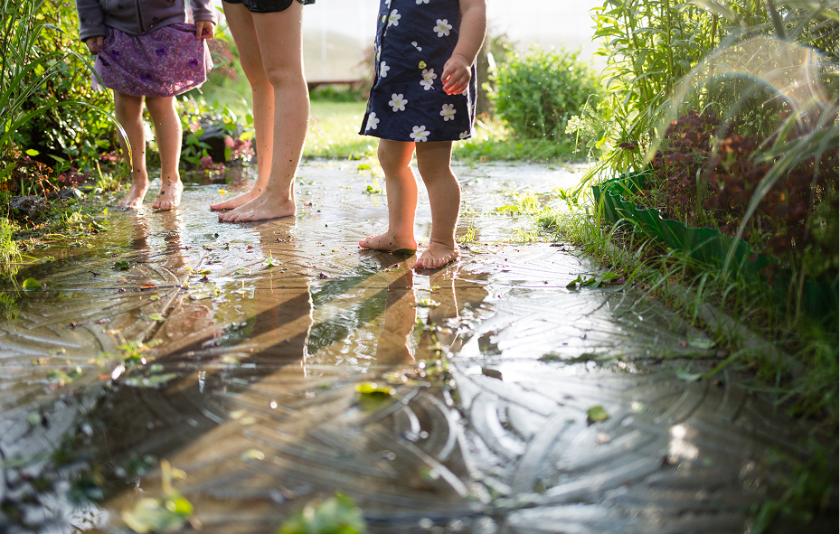 Barefoot children standing on a wet garden path with reflections in the puddles