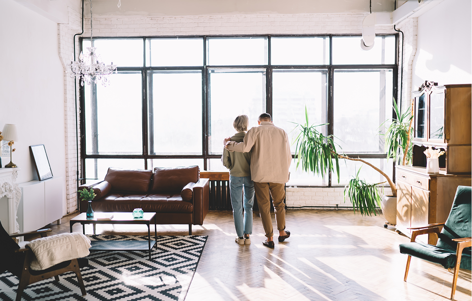 Couple standing with their backs to the camera looking out of large windows in a spacious, sunlit modern living room