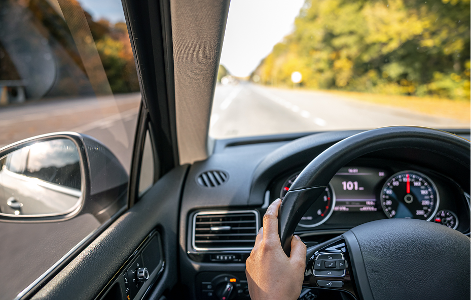 Driver's hand on a car steering wheel driving down an open highway
