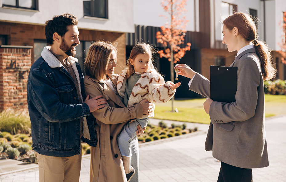 Real estate agent handing keys to a family of three in front of their new home