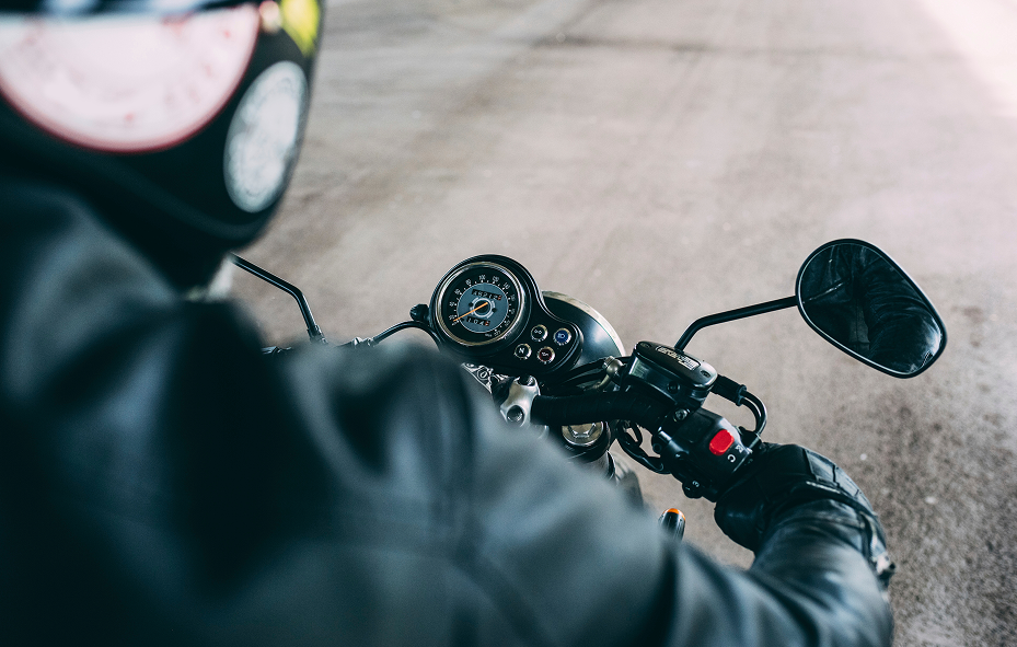 Close-up over-the-shoulder view of a motorcycle rider’s hand on the handlebar while riding