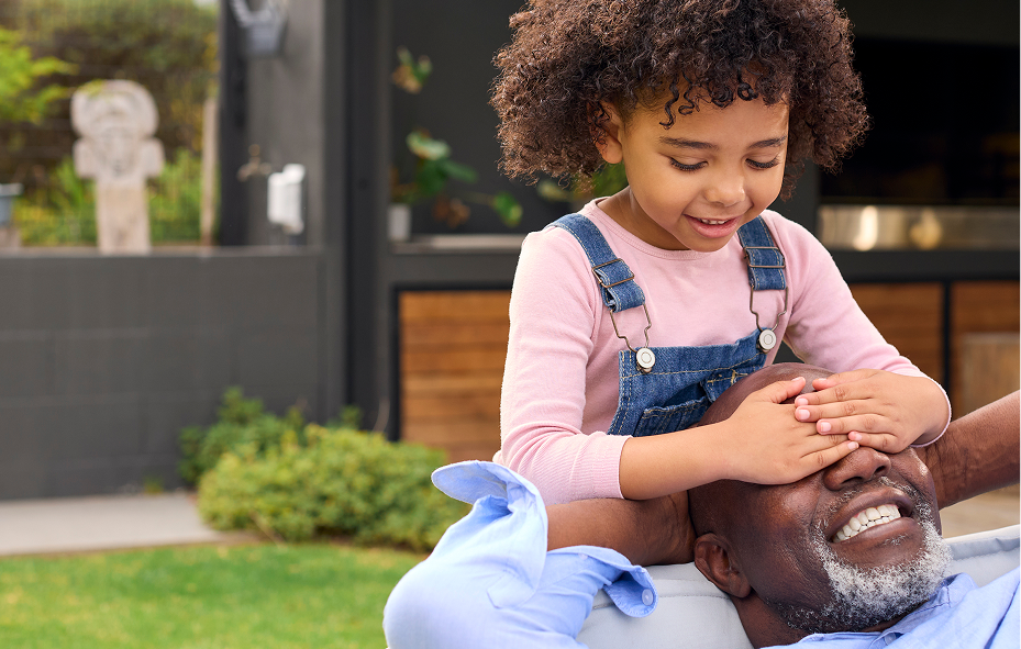 Happy young girl covering her grandfather's eyes in a playful moment outdoors