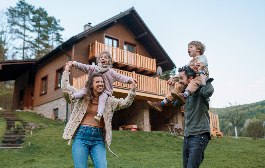 Happy family looking up at a rustic, multi-story wooden cabin nestled in a grassy field
