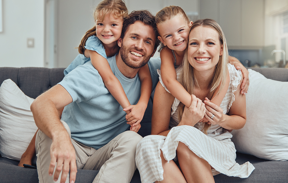 Happy smiling family of four with two young boys sitting together on a couch