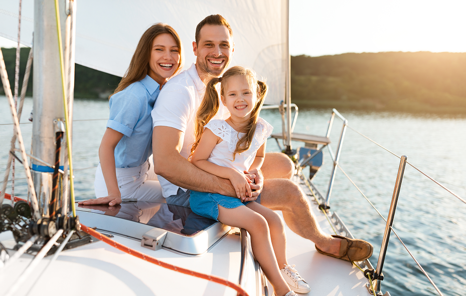 Happy family of three smiling together on a sailboat at sunset