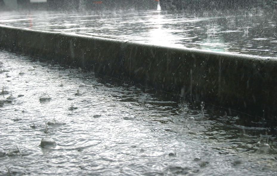 Heavy rain falling and splashing on a flooded pavement next to a concrete curb