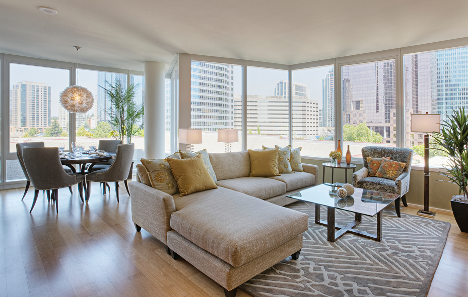 Bright, modern apartment living room with a sectional sofa and large windows overlooking a city skyline