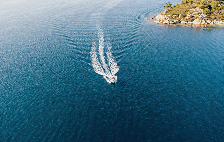 Aerial view of a small boat cruising on deep blue water near a rocky shoreline