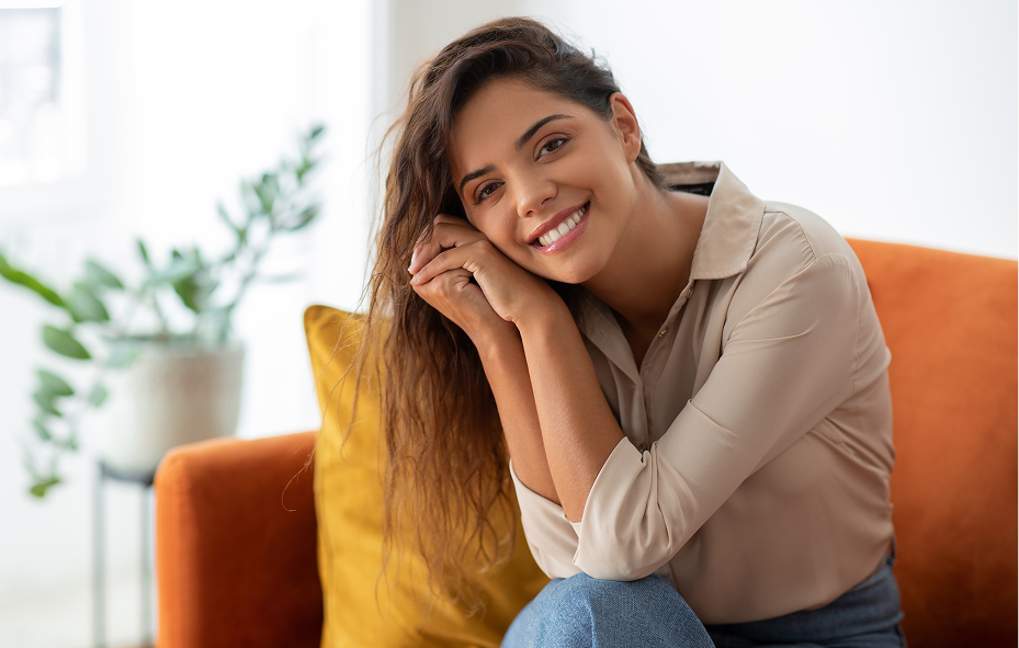 Happy smiling woman sitting on a comfortable orange sofa with yellow cushions